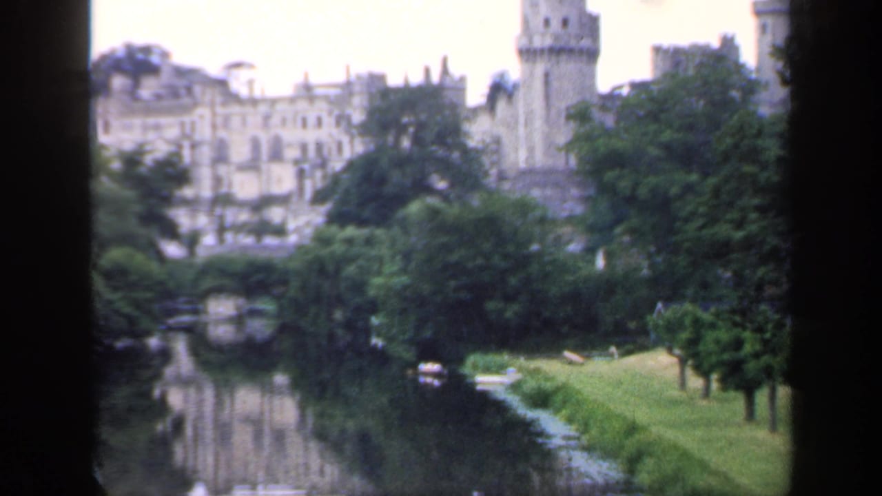 1949 England home-movie view of a castle-like stone building and tower across a calm river, framed by dark vertical edges.