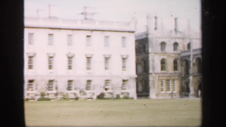 Final 1949 England frame showing a white building wing, adjacent arched stone facade, lawn foreground, and home-movie softness.