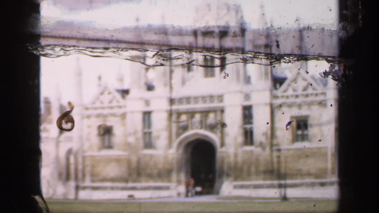 Soft 8mm frame of a Gothic stone building seen across a lawn with dark film borders.