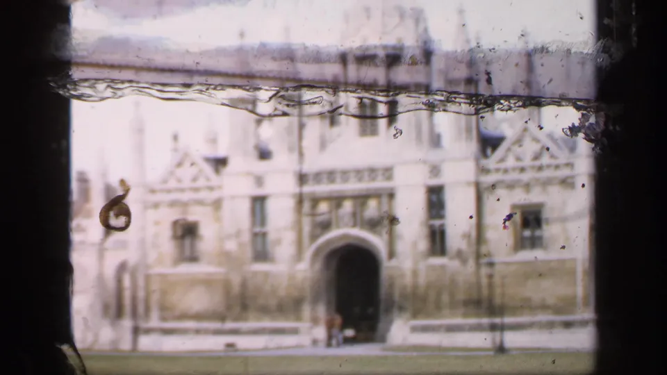 Late-1940s England home-movie frame showing a pale Gothic stone facade and arched entrance across a green lawn.