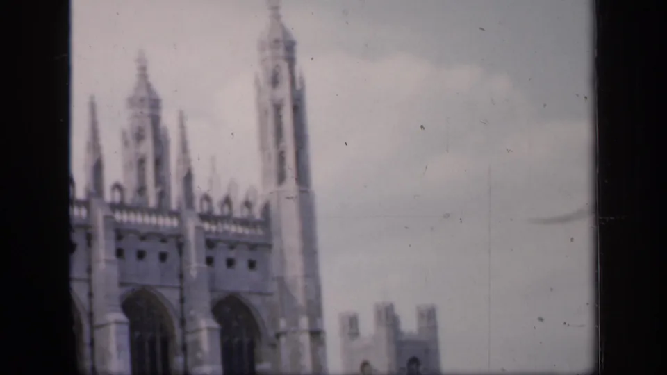 Soft 8mm frame from England in 1949 showing a Gothic cathedral facade with spires, tall windows, pale sky, and a distant square tower.