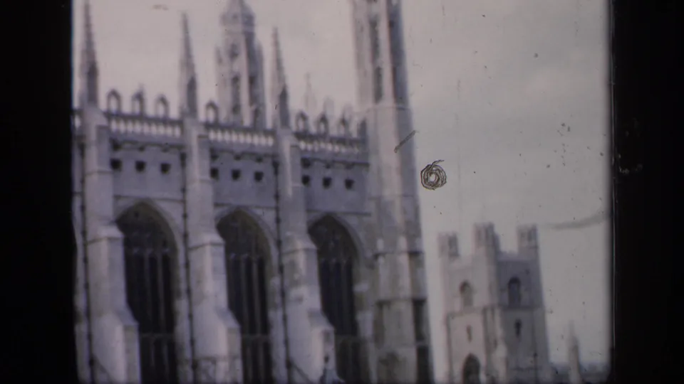 1949 England home-movie frame showing a pale stone Gothic cathedral exterior, high arched windows, spires, and a tower beyond the main structure.