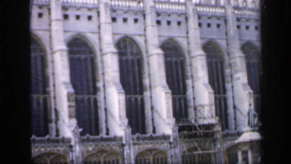 1949 England frame with repeated pointed windows on a pale Gothic church facade, scaffolding at the lower level, and a small figure near a pedestal.
