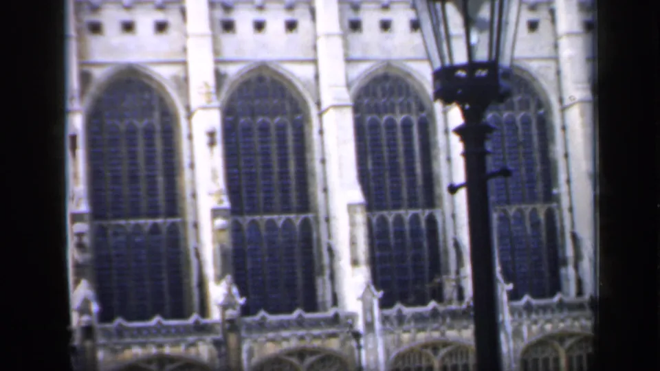 1949 England 8mm frame of pale Gothic cathedral stonework, repeated pointed windows, and a dark lamppost at the right edge.