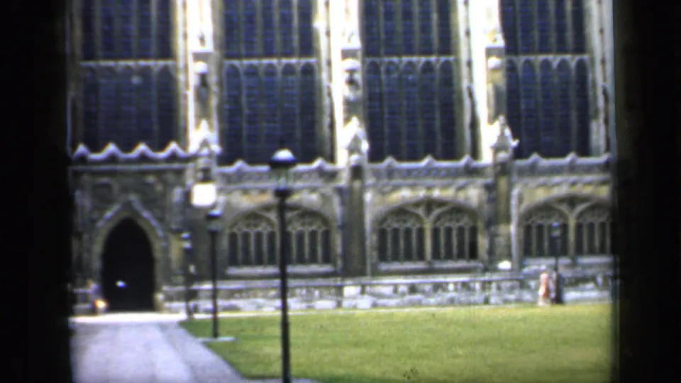 Final 1949 England frame showing the church facade, dark doorway, paved approach, lawn, lampposts, and distant people.