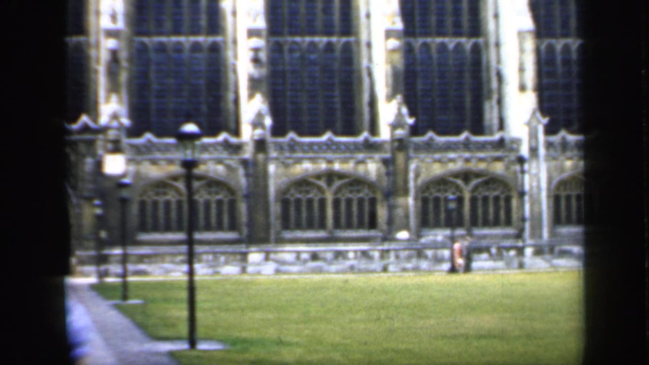 Gothic stone facade across a lawn, seen past dark window framing and a lamppost.