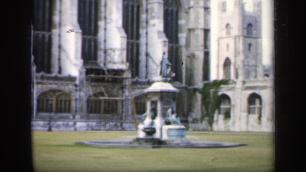 Grassy courtyard with a fountain before a tall Gothic stone building.