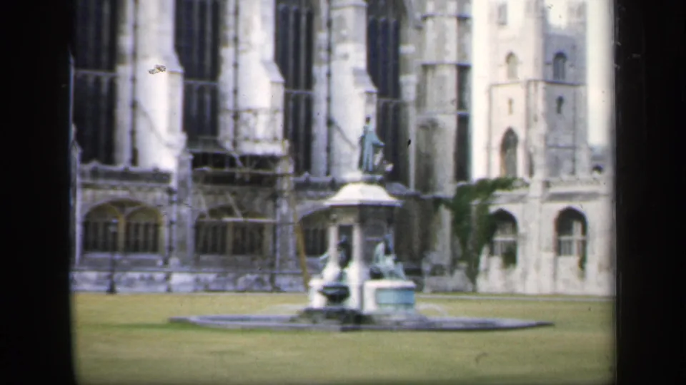 1949 England home-movie view of a courtyard fountain in front of a historic Gothic stone facade with tall arched windows.