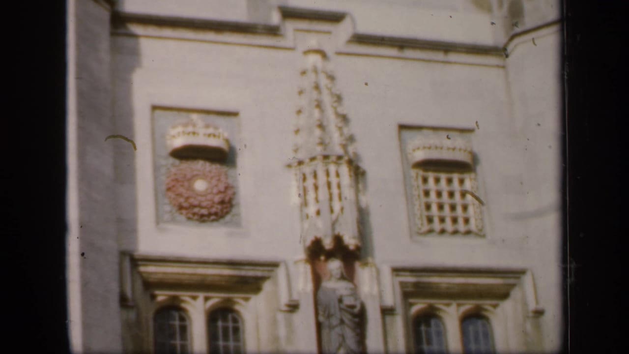 Close 1949 England view of carved stonework, a statue niche, arched windows, and crest-like ornament on a historic building facade.