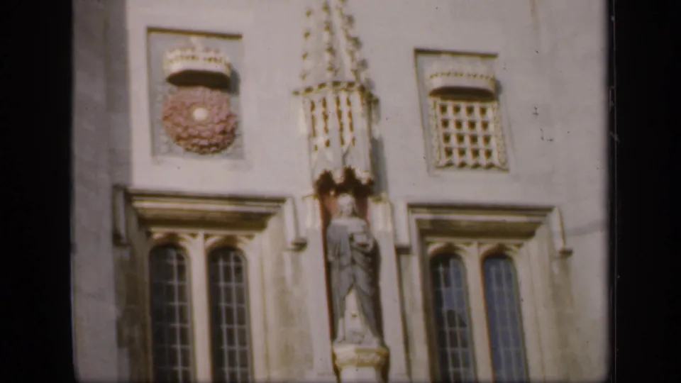 Soft 8mm frame of an English historic facade with arched windows, decorative crest, lattice window, and a carved statue niche.