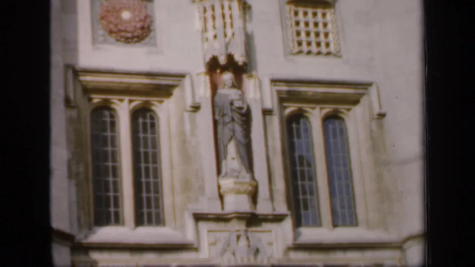 1949 England close view of a carved statue set into a historic stone facade between tall arched windows and decorative stonework.