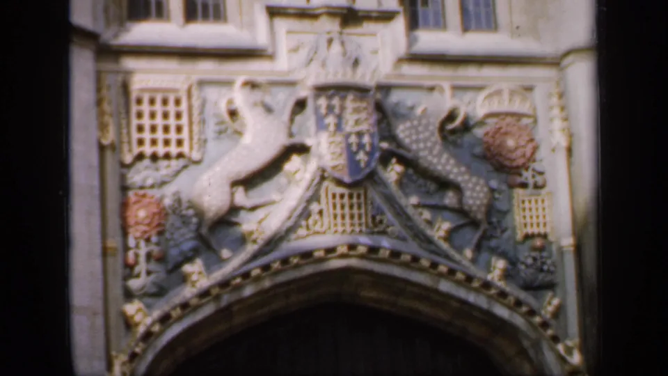 1949 England home-movie frame showing carved heraldic animals, shield details, and floral motifs over a dark doorway.