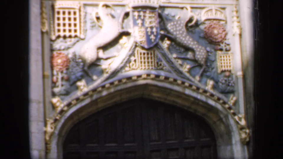 1949 England frame centered on the carved coat of arms and decorative stonework above a dark arched wooden door.