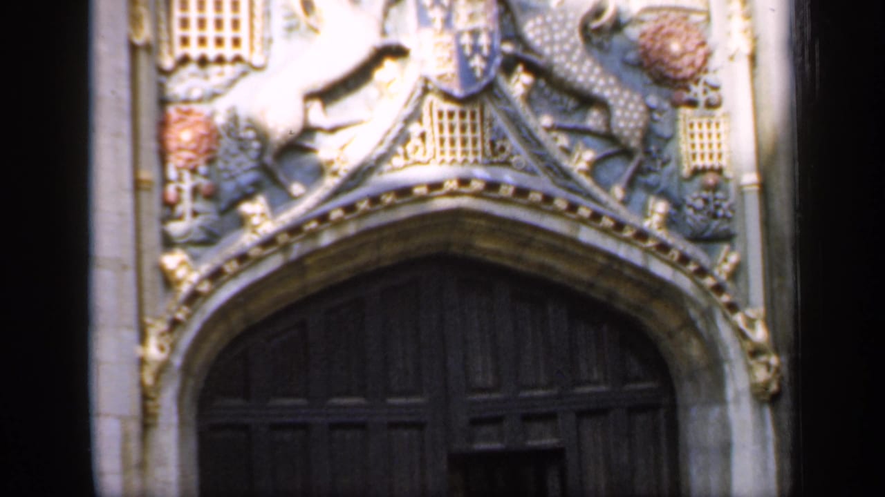 1949 England home-movie frame showing carved stonework and heraldic details above a large dark wooden cathedral door.