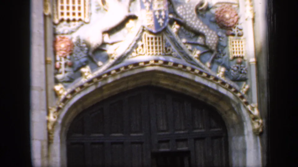 1949 England home-movie frame showing carved stonework and heraldic details above a large dark wooden cathedral door.