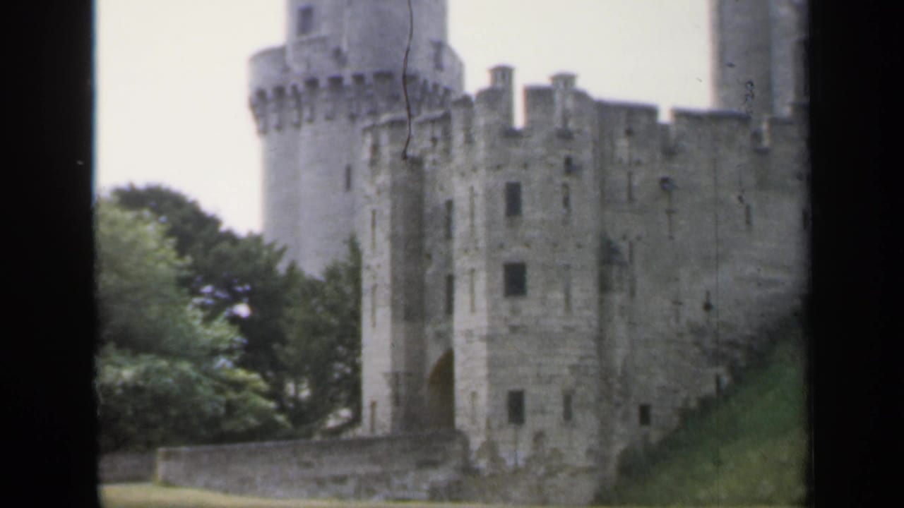 Medieval stone castle exterior with round towers, battlements, and trees.
