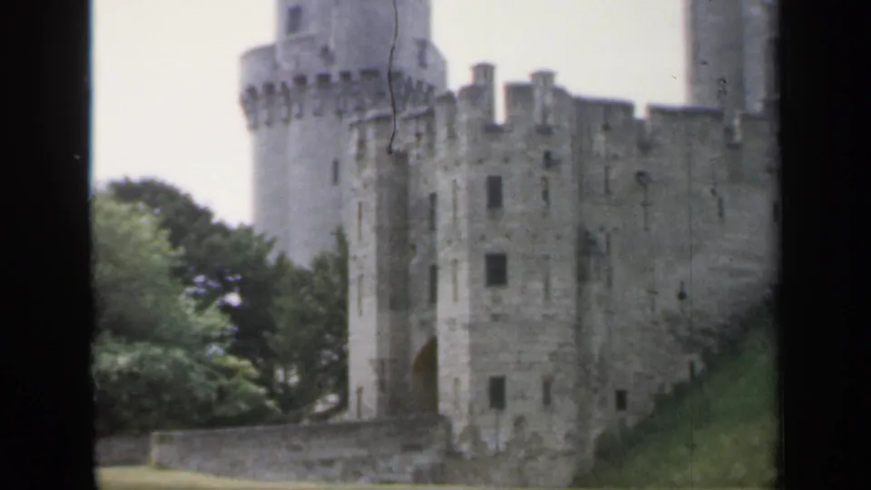 1949 England 8mm view of a medieval-style stone castle exterior with towers, battlements, trees, and a sloped foreground.