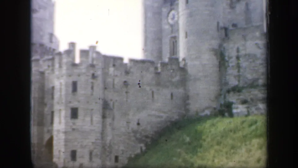 1949 England 8mm view of the castle facade and battlements, with a tower edge, small windows, and a green sloped foreground.