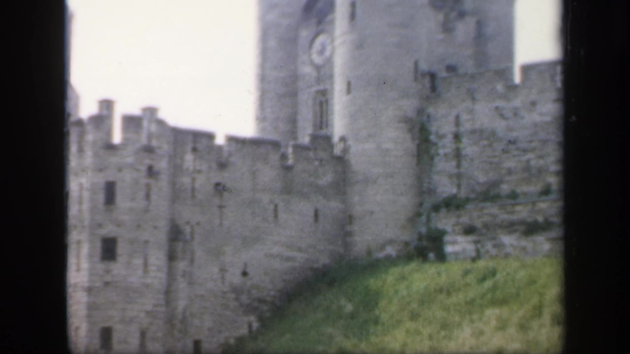 1949 England home-movie view of a gray stone castle with battlements, a clock tower and grass in the foreground.
