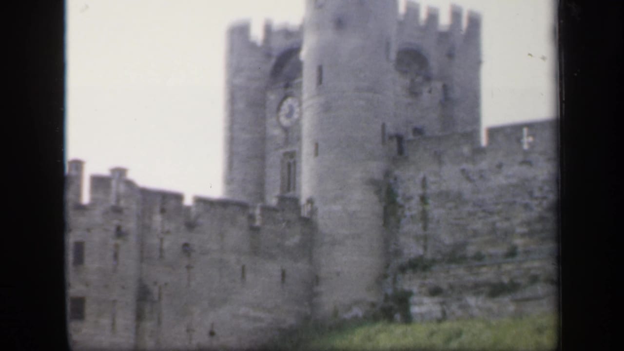 The camera holds on the castle exterior, showing the clock tower, gray battlements and grassy hillside in 1949 England.