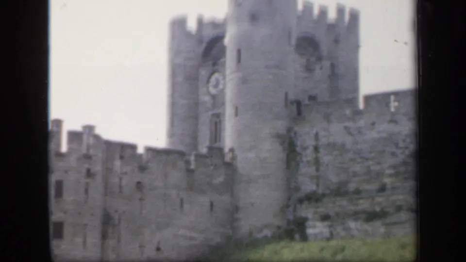 The camera holds on the castle exterior, showing the clock tower, gray battlements and grassy hillside in 1949 England.