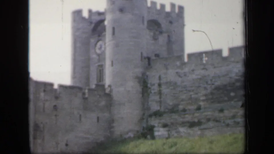 Soft 8mm frame of the English castle exterior, centered on the tower, clock face and adjoining crenellated stonework.