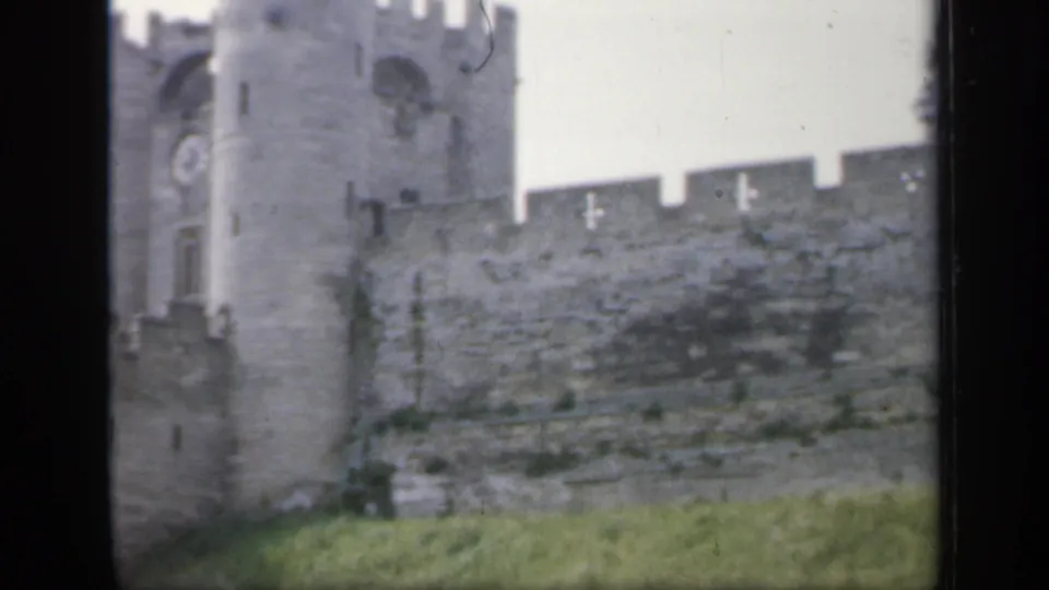 Final frame shows the castle wall and tower above green grass, with muted 8mm color and visible film-frame edges.