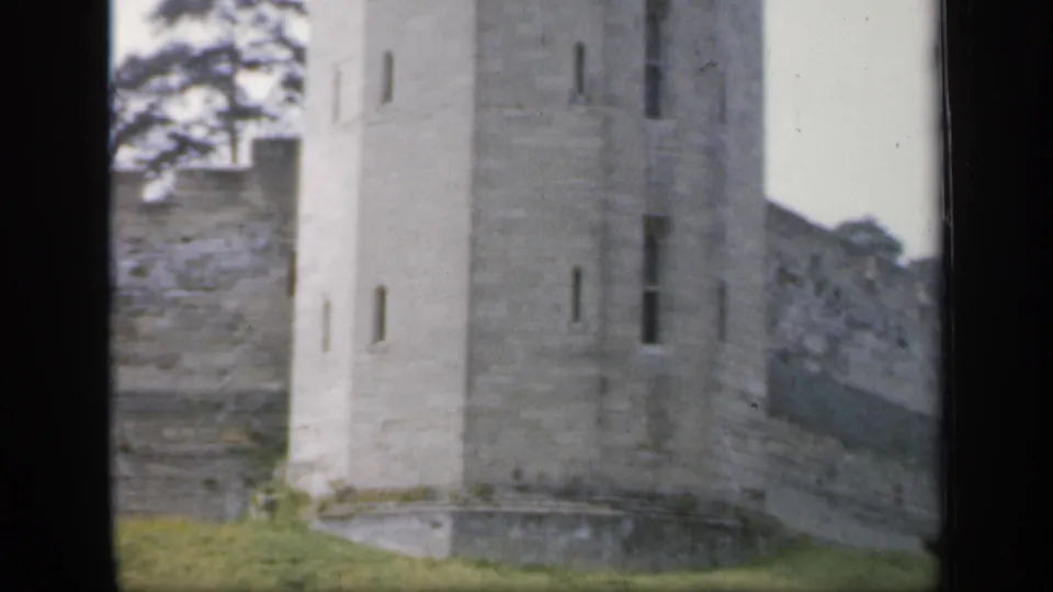 1949 England 8mm view of a gray stone tower with narrow windows, adjoining wall, grass, and visible scan border.