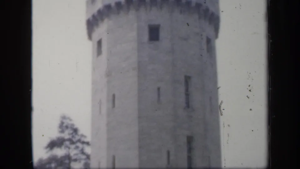 1949 England 8mm frame showing a round stone tower with crenellations, small window openings, trees, and soft daylight.