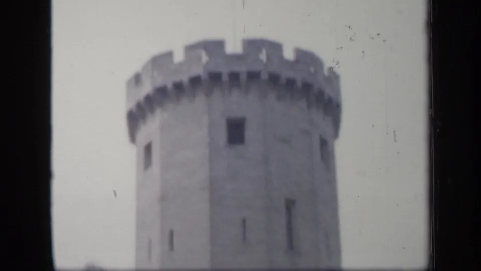 1949 England 8mm frame focusing on the upper portion of a round crenellated stone tower against a pale sky.