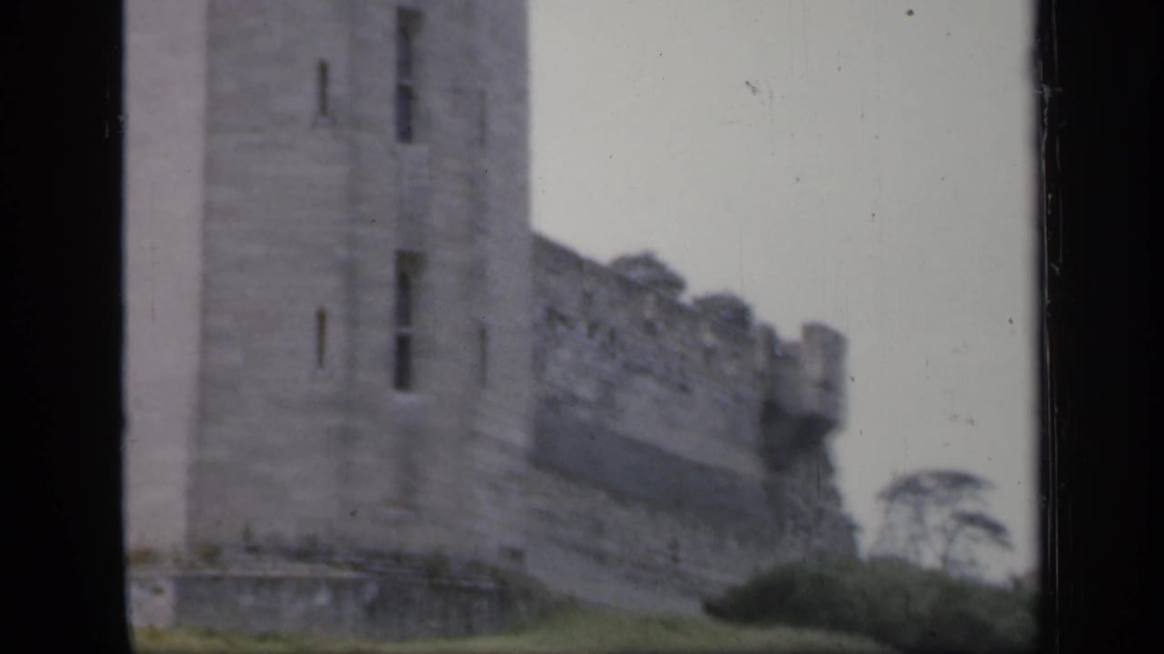 Rectangular castle tower and adjoining crenellated wall above a grassy bank.