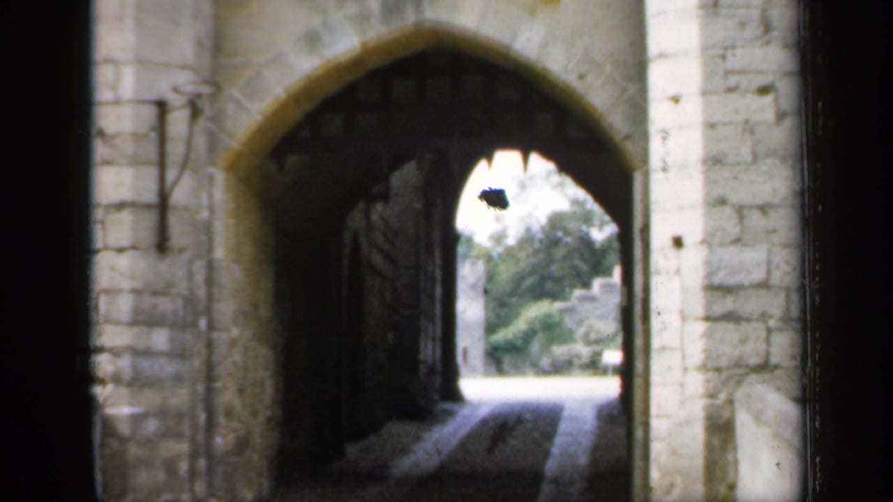 1949 England home-movie still of a shadowed stone archway and open iron gate leading toward a bright outdoor area.