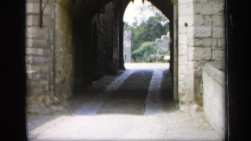 Final 1949 England frame showing the castle passage opening, stonework, open iron gate, trees, and a stone feature near the exit.