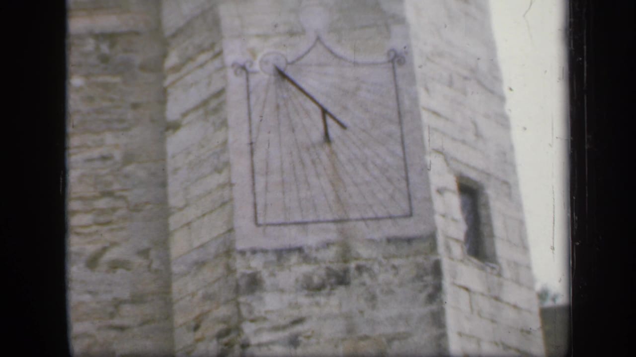 1949 England 8mm frame showing an exterior sundial mounted on a weathered stone wall.