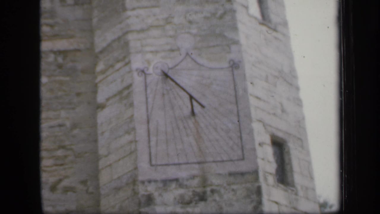 1949 England frame with a sundial centered on rough stonework and a narrow side wall visible.