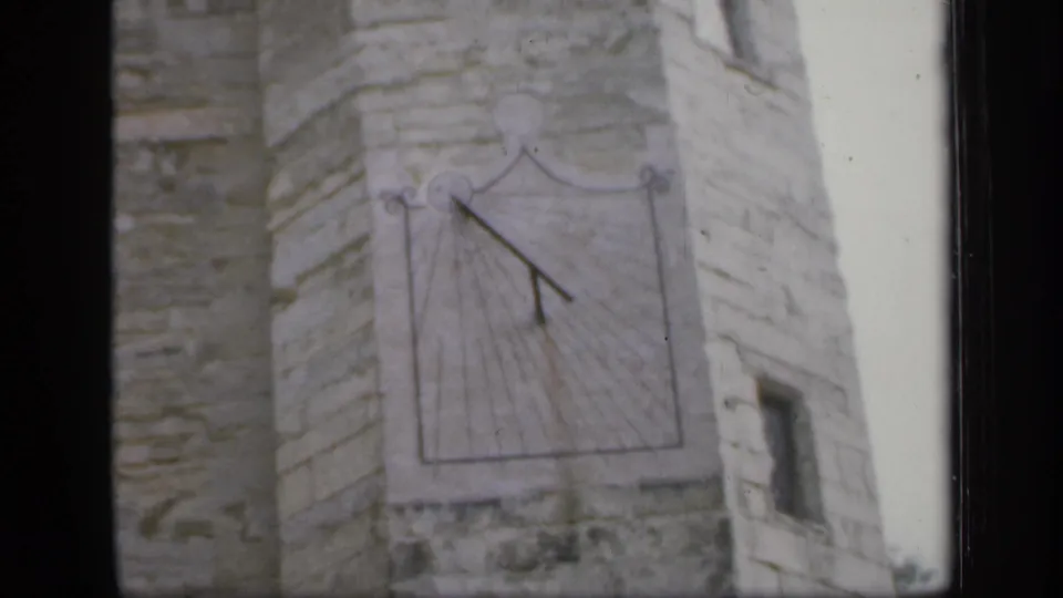1949 England frame with a sundial centered on rough stonework and a narrow side wall visible.