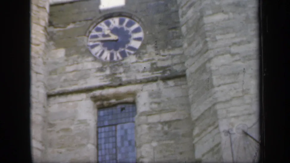 1949 England frame with the castle clock face high on the stone wall and a leaded window below.