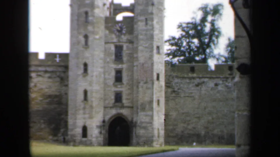 1949 England home-movie view of the castle entrance with tower, arched gateway, crenellated wall, trees, and grass.