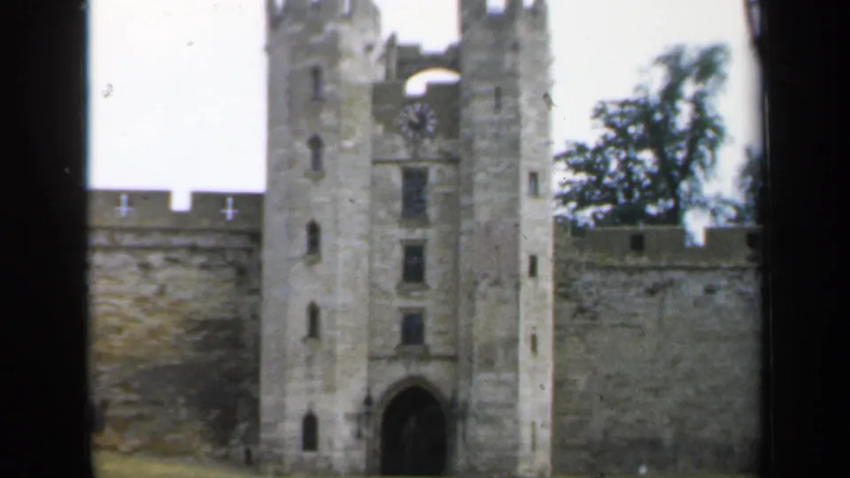 1949 England frame showing the castle entrance tower and arched gateway framed by walls, trees, and grass.