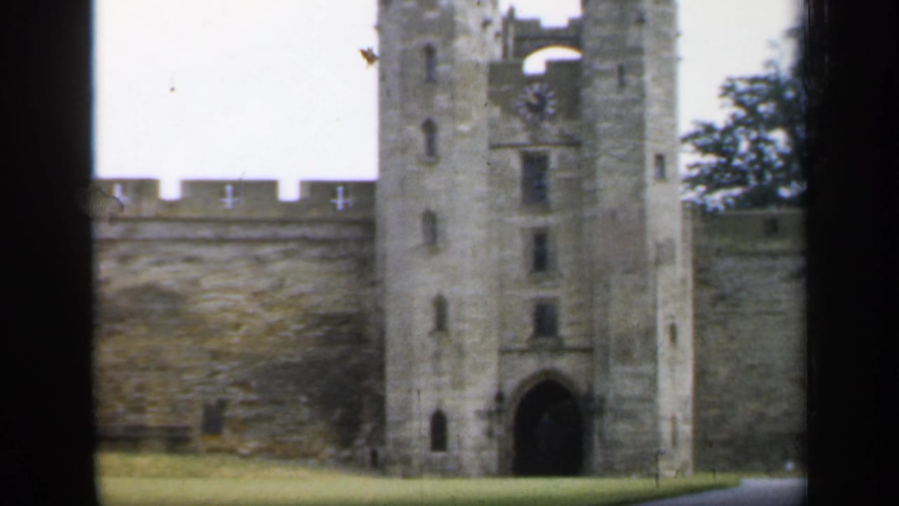 1949 England home-movie view of castle towers, crenellated wall, arched gateway, and lawn seen through dark vertical framing.