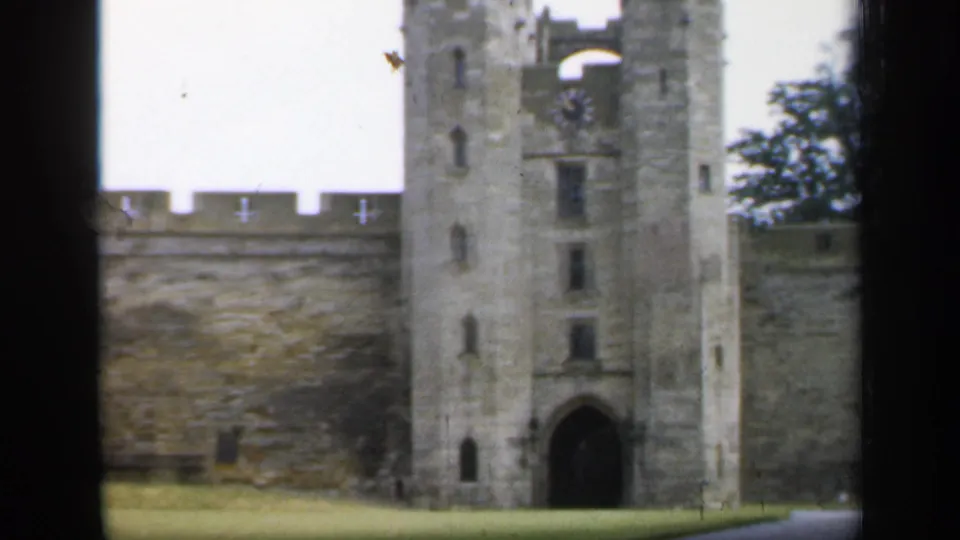1949 England home-movie view of castle towers, crenellated wall, arched gateway, and lawn seen through dark vertical framing.