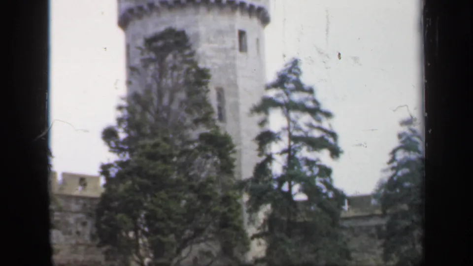 1949 England home-movie frame showing a round castle tower, wall, and trees in soft focus.
