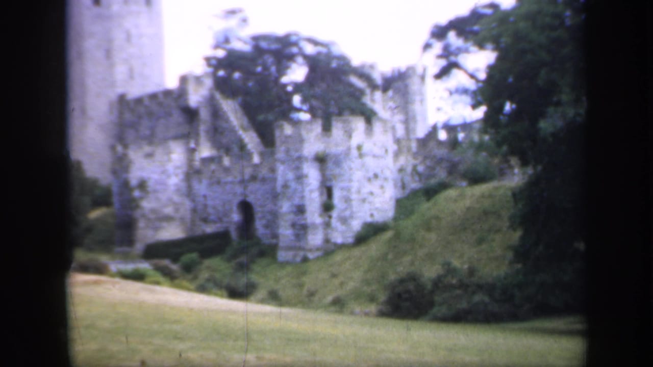Stone castle walls and a round tower above green lawns and trees.