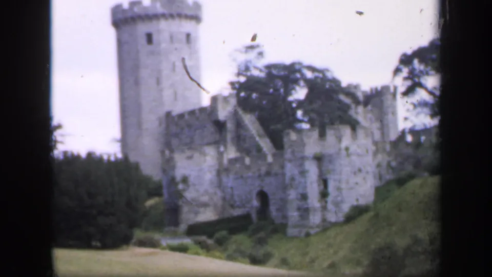 Soft 8mm frame from 1949 England showing a closer castle view with tower, weathered masonry, lawn, and surrounding trees.
