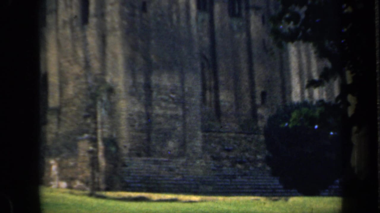 1949 England home-movie view of a weathered castle wall, grassy ground, and shaded foreground framing.