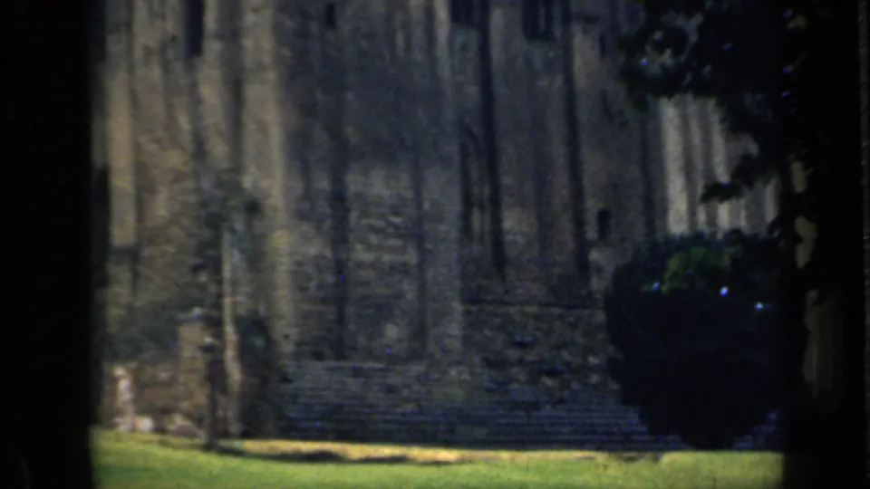 1949 England home-movie view of a weathered castle wall, grassy ground, and shaded foreground framing.