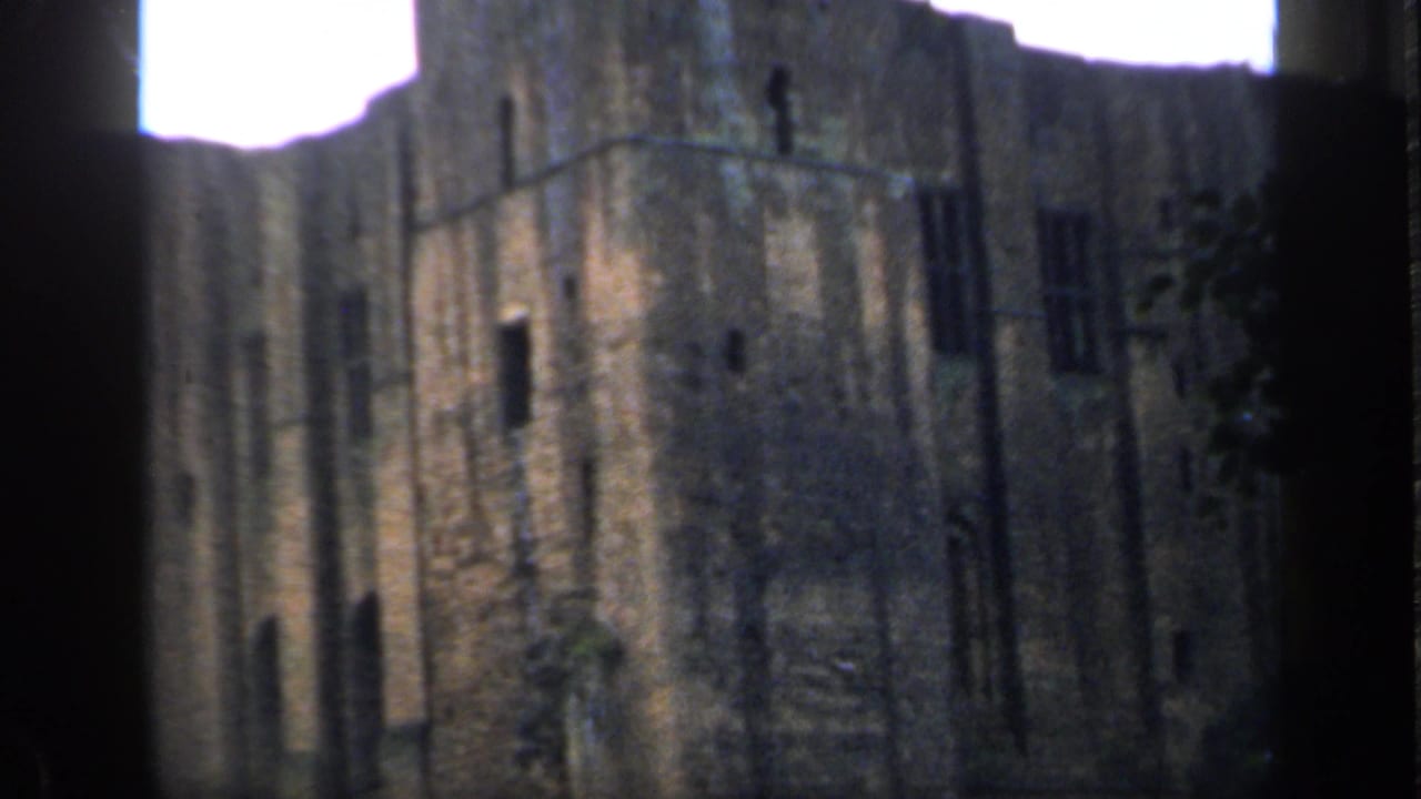 Tall English castle ruin filmed in 1949, with narrow dark openings and overexposed sky behind the wall.