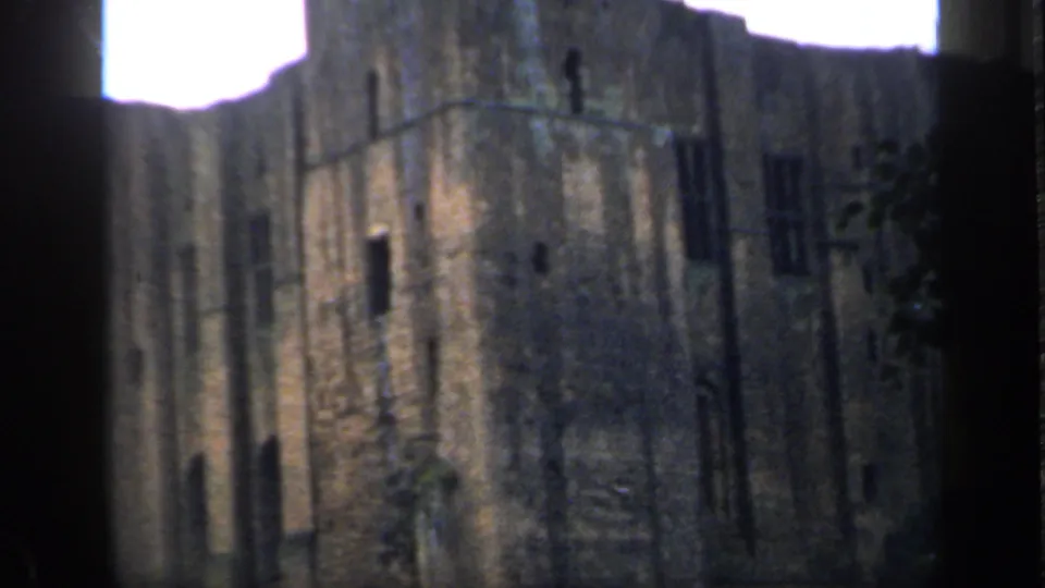 Tall English castle ruin filmed in 1949, with narrow dark openings and overexposed sky behind the wall.