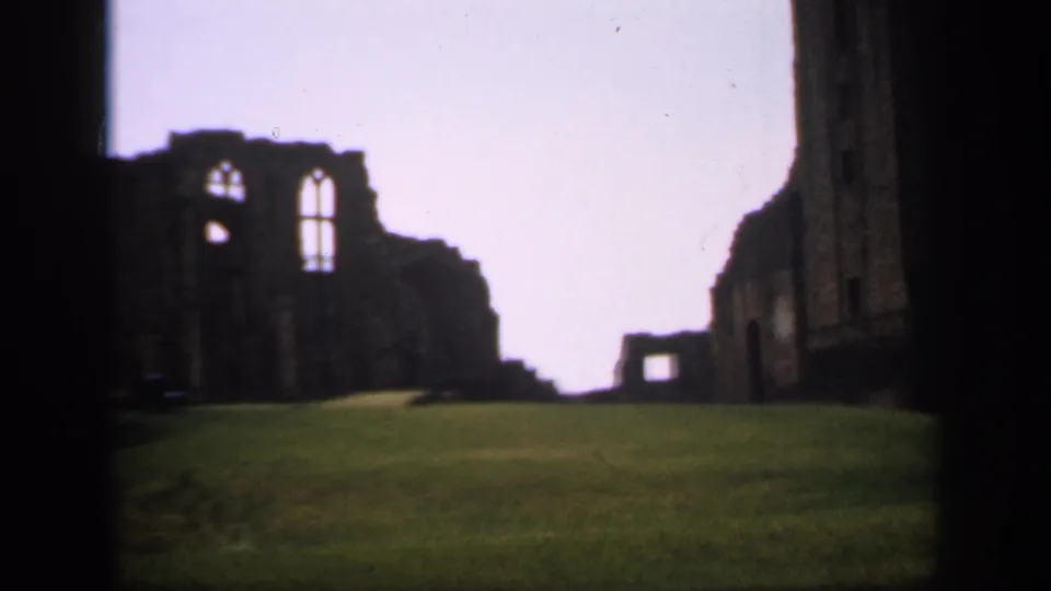 1949 England 8mm frame centered on weathered stone ruins with large Gothic-style window openings above a sloped lawn.