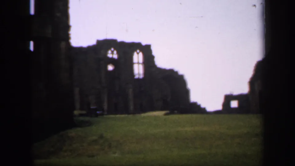 1949 England 8mm frame showing arched window openings in a stone ruin, with grass in front and dark masonry along one side.